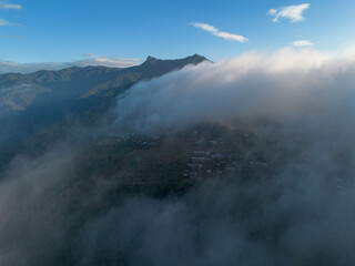 Fototapeta premium A high-angle landscape, a village in the middle of mountains surrounded by white fog. Beautiful landscapes, villages in the middle of forests, green mountains, clear skies. Photos from a drone