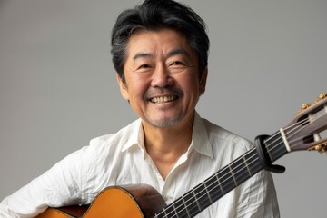 Portrait of a grinning asian man in his 40s playing the guitar over soft gray background