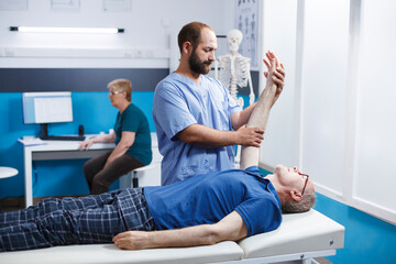 Chiropractor in blue scrubs uses osteopathic massage to help elderly male patient heal their hand muscles. Medical nurse helps old man extend his arm joint as part of his physical therapy.