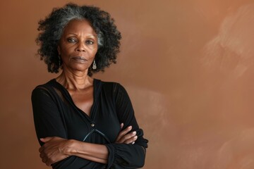 Portrait of a tender afro-american woman in her 50s with arms crossed on soft brown background
