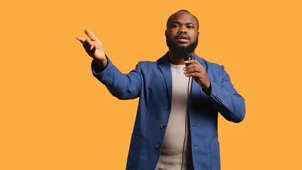 African american motivational speaker holding monologue using microphone, gesturing with hands, studio background. Energetic BIPOC speaker talking during presentation using mic, doing speech, camera B
