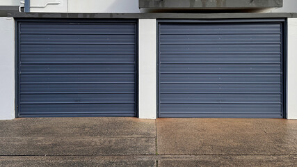 two grey color metal garage doors with horizontal lines against white building with concrete driveway