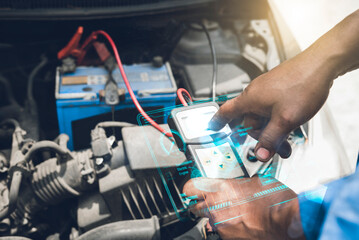 Mechanic uses a diagnostic tool to check a car engine's battery and electrical system for issues in a garage.