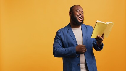 Man laughing while reading funny book, entertained by engrossing story. Joyful person having fun,...