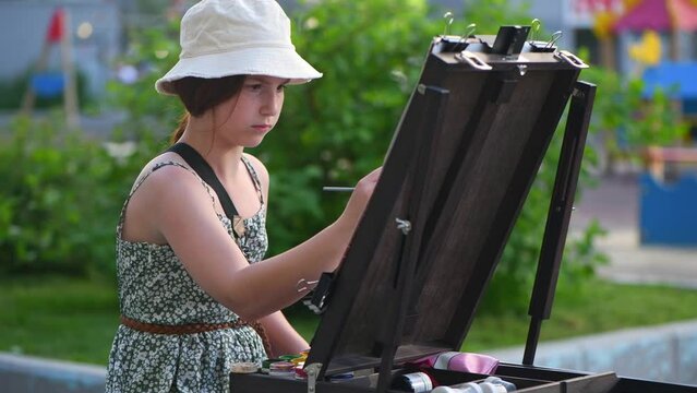 Cute teenage girl drawing at easel outdoors, in the courtyard of the house in the city, art, plein air