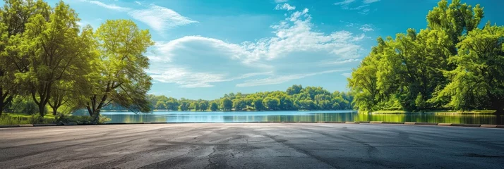 Gordijnen Empty asphalt road and green trees with blue sky background over the lake in summer, landscape nature view from side of empty street for product display. © Oulaphone