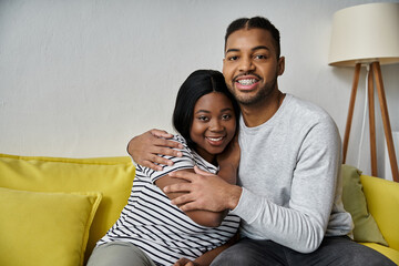 Obraz premium An African American couple sits on a couch, smiling and embracing each other.