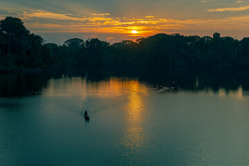 Silhouette of a man paddling a canoe in the Amazon rainforest at sunrise, Yasuni national park,...