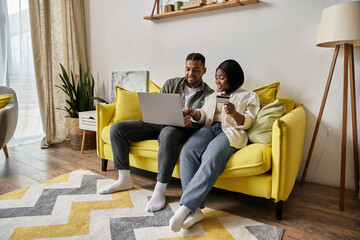 African american couple shops online, relaxes on yellow sofa.