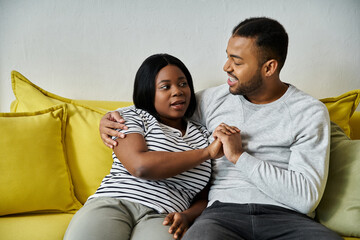 Fototapeta premium An African American couple sits together on a couch, holding hands and talking.