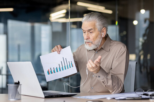 Senior businessman holding a chart during an online video conference in a modern office setting, discussing business data and analytics. - Powered by Adobe