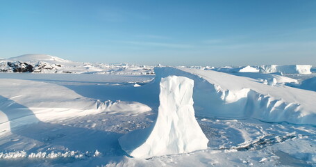 Snow-covered arctic winter landscape with towering glacier in pristine icy landscape. Beauty Antarctica nature. Many icebergs stuck in frozen ocean. Blue sky sunny day. Aerial view drone shot panorama