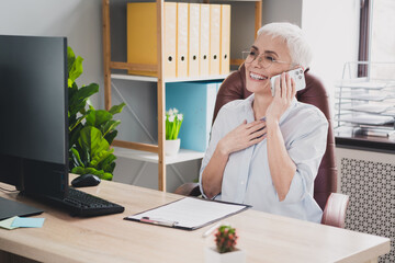 Photo of smiling positive mature lady specialist formalwear talking modern device indoors workplace...