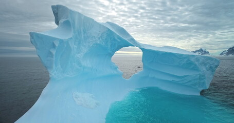 Giant blue melting iceberg with cave drifts ocean water. Drone fly inside ice glacier hole. Polar nature. Cold South Pole winter landscape. Wild nature people explore travel. Cinematic ecology scene.