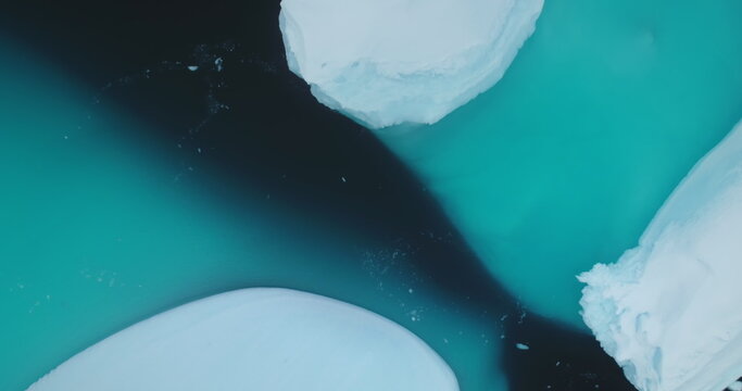 A collection of icebergs drift cold arctic water surface. Ice formations in natural winter landscape. Melting glaciers in Antarctica. Global warming, climate change. Aerial view top down drone shot