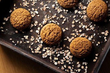 Craft and rustic four oatmeal cookies. Dark food aesthetics, black background with several oat flakes.