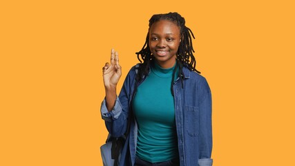Smiling african american student at school raising arm to answer question, isolated over studio background. Cheerful girl with hand up volunteering to tell teacher explanation to question, camera A