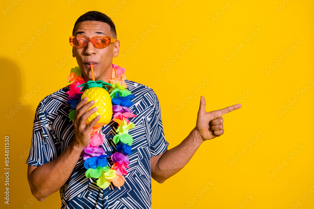 Wall mural Photo of attractive funny guy wear print shirt hawaii necklace enjoy fruit juice showing emtpy space isolated yellow color background