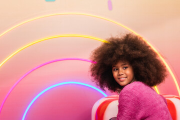 Teenage girl in colorful studio. Side view of black teenage girl with Afro hairstyle looking away in vivid studio with colorful illuminated lamps