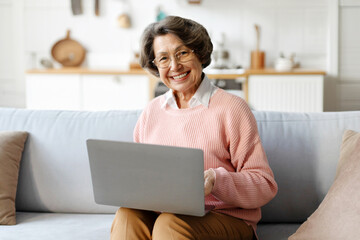 Happy elderly good-looking woman using laptop online for remote shopping or paying domestic bills...