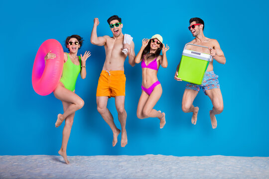 Full length photo of lucky excited fellows company wear swimsuits jumping high celebrating journey isolated blue color background