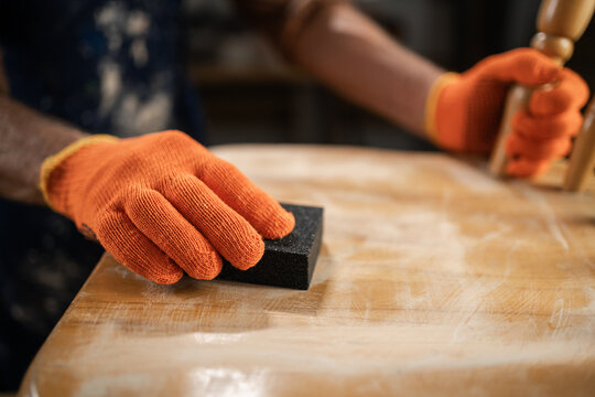 furniture repair, DIY and home improvement concept. man in orange gloves sanding wooden chair with sandpaper, preparing surface for further processing.