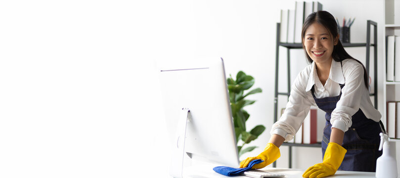 Young Asian cleaning woman uses a cloth to wipe clean a computer and keyboard using cleaning solution in her home office.