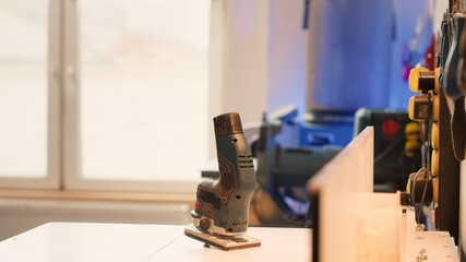 Close up of electric router on spindle moulder in furniture assembly shop with woodworking tools on rack in background. Focus on hand powered equipment used for sanding wood in studio, panning shot