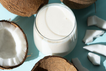 Coconut milk in a glass among coconuts on a blue background