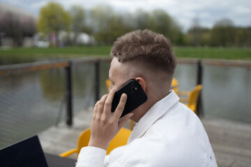 Happy successful European businessman makes a phone call on smartphone, talking and smiling outdoors sits at city cafe on city street outside. High quality FullHD footage