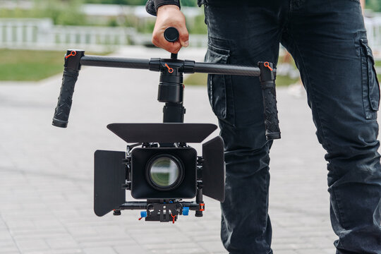 videographer working outdoors in park with video camera set on steadycam, cameraman at work