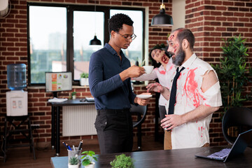 Fatigued office workers stressed by overworking turning them into zombies, asking manager to lessen burden. Tired employees in tense conversation with boss, unhappy with relentless corporate demands