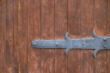 An old-style door hinge on a wooden gate made of old panels painted in brown as a vintage background