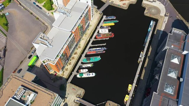 Aerial drone footage of the area in the Leeds City Centre known as The Leeds Dock showing rows of long boats and narrowboat dutch barges on a sunny day in the summer time