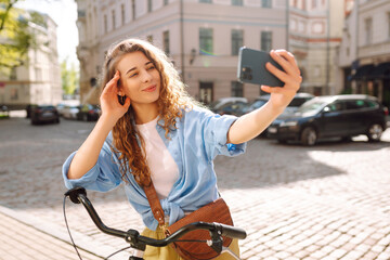 Attractive woman taking selfie with bike on the street of old European city. Communication with friends and family remotely. Selfie time.