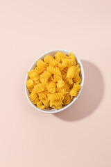 Close-up of a bowl filled with uncooked fusilli pasta spirals on a pink background