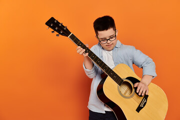 Naklejka premium A young boy plays the guitar in front of an orange background.