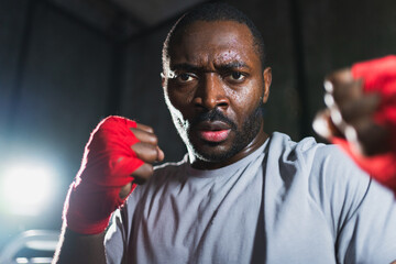 Boxer in gym. Aggressive African man fighter resting after training boxing ready for fight looking at camera. Strong sweated man training punches looking concentrated straight preparing for sparring