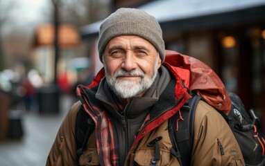 Obraz premium A man wearing a brown jacket and a gray hat is smiling. He is carrying a backpack and a handbag