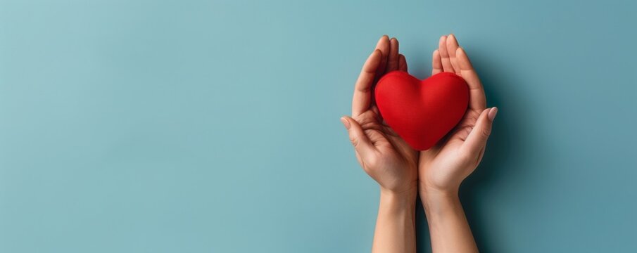 Two hands gently hold a red heart on a blue background