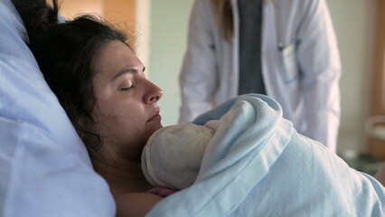 New mother struggling with pain after childbirth laid in bed being taken care by medical team,...