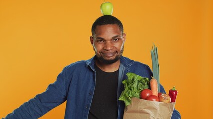 Playful vegan guy dancing with an apple placed on his head, having fun trying to be balanced and not drop it. Confident happy man recommending homegrown local fresh produce. Camera A.