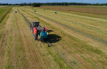 Obraz premium Schwarzer Treker oder Traktor mit einer roten Stroh Festkammerpresse bei der Strohernte auf einem gemähten Feld