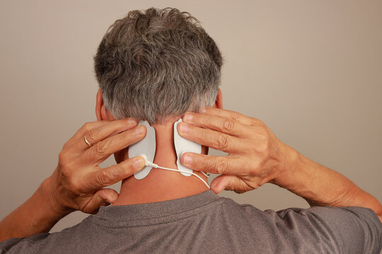 Man using a Electro Therapy Massager or Tens Unit on the back of his neck for pain relief for a migraine headache 