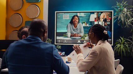 Project management team attending videocall meeting with shareholders, creating a presentation to review updates and data reports. Employees discuss remotely with executive board members. Camera B.