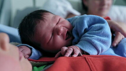 Newborn baby resting on older sibling's chest, looking alert with mother in background, capturing a...