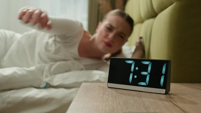Angry annoyed tired exhausted girl wake up in morning bed home bedroom woman female lady anger mad furious loud sound ringing of alarm clock awaking early beat off alarmclock continue sleep insomnia