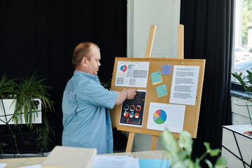A man with inclusivity is presenting data on a corkboard in a modern office setting.