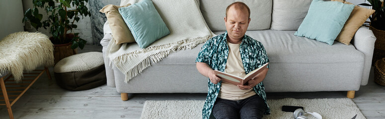A man with inclusivity sits on a sofa, engrossed in a book, enjoying a quiet moment of relaxation.