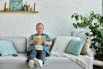 A man with inclusivity relaxes on a couch, engrossed in a book, enjoying a moment of peace.
